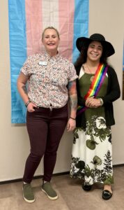 A picture of two people in front of the transgender pride flag. On the right is Noel, GA Equality staff member, and on the left is Marisol Payero.